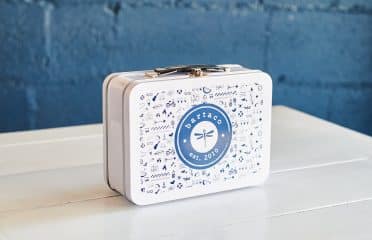 image of the exterior of the bartaco kids lunch box. white metal lunch box with blue hand-drawn bartaco illustrations