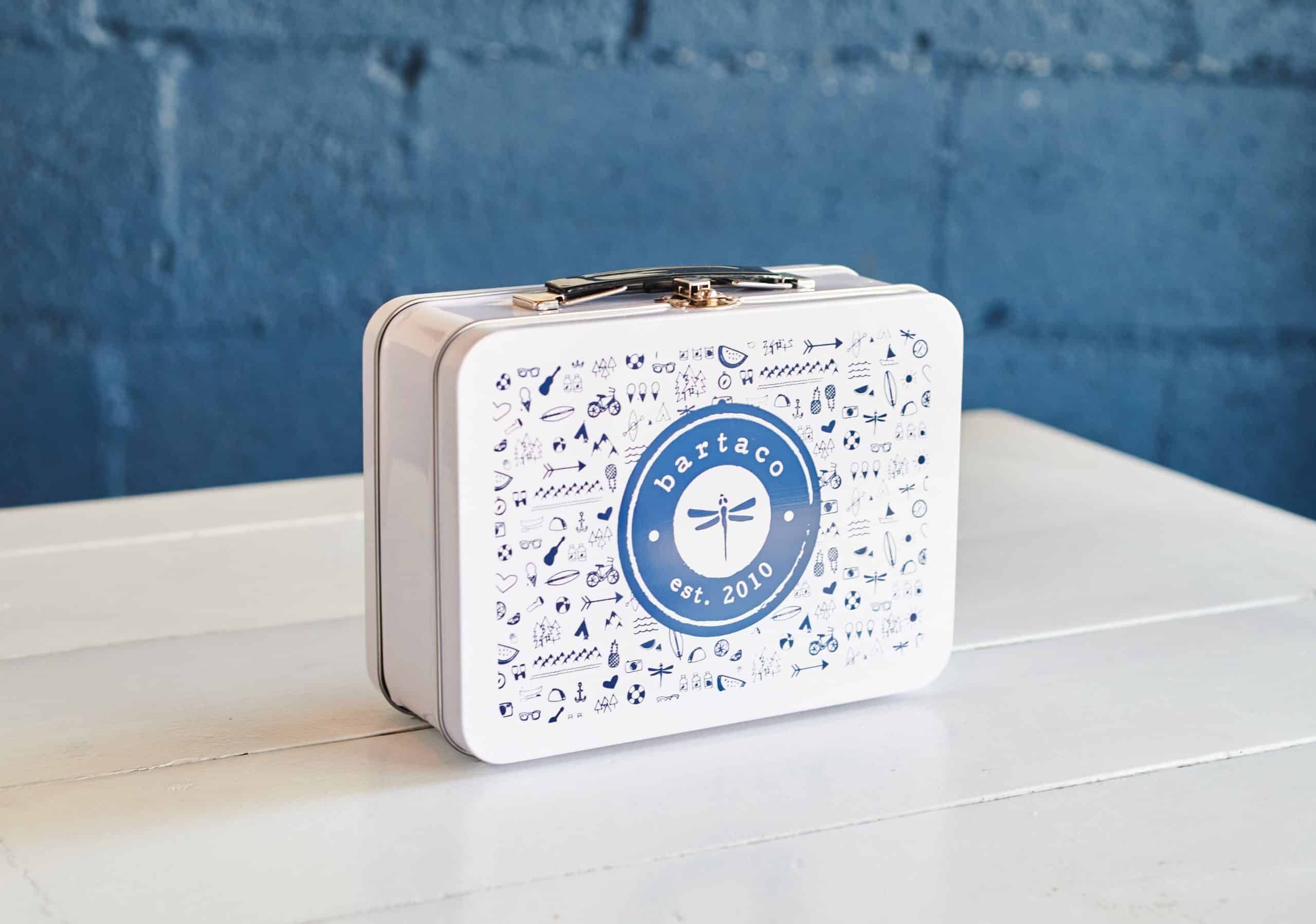 image of the exterior of the bartaco kids lunch box. white metal lunch box with blue hand-drawn bartaco illustrations