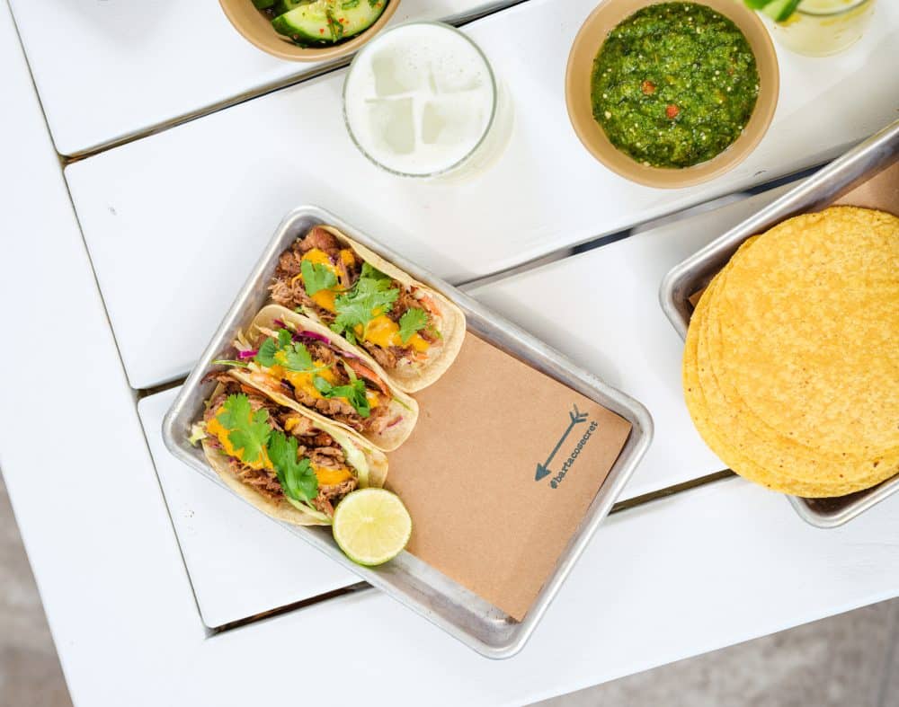 table with tray of three #bartacosecret slow-roasted pork tacos