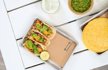 table with tray of three #bartacosecret slow-roasted pork tacos
